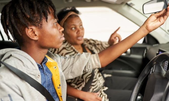 Photograph of a female driving instructor instructing a male learner driver in a car