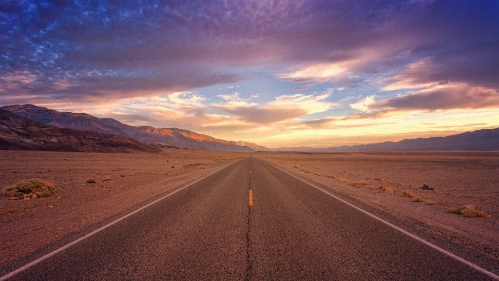 Photograph of a long, clear desert highway going into the sunset