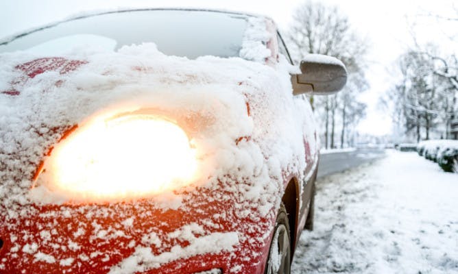 A car covered in snow, the camera focused on a headlight