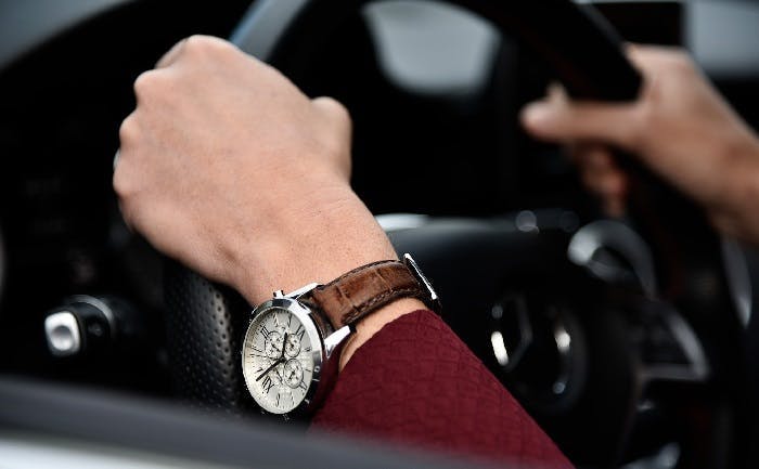 Hands with watch holding steering wheel