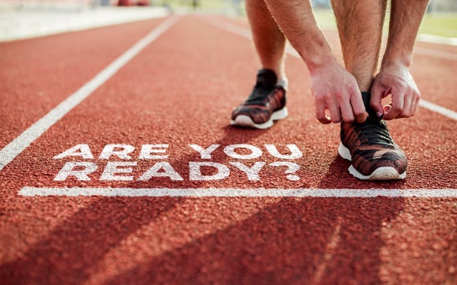 A runner tying their laces at their mark, which says "Are You Ready?"