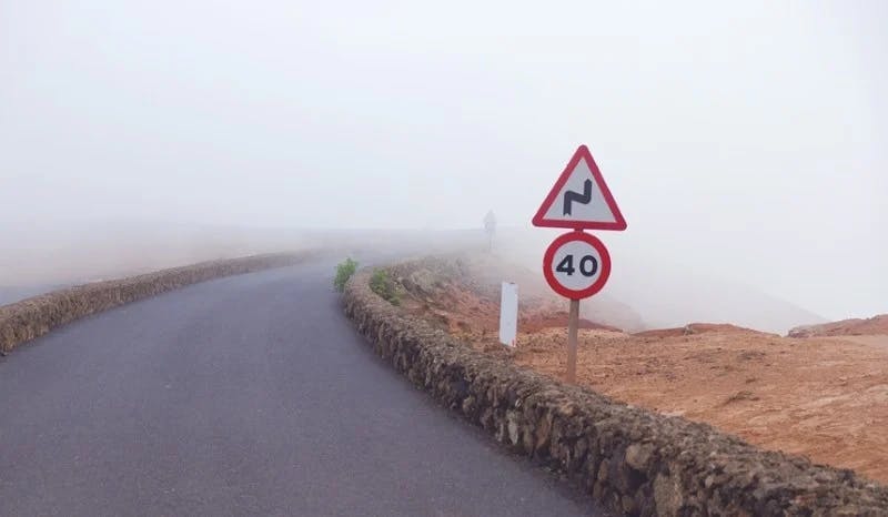 A speed limit sign and a bend sign on a foggy road