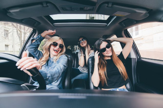 A group of female friends smiling and dancing in a car