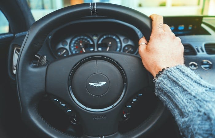 One hand on Aston Martin steering wheel