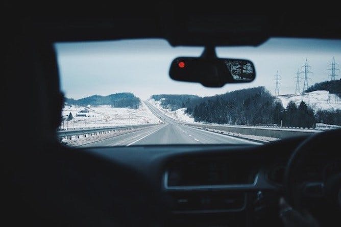 An image from the inside of a car with a road and snowy mountains shown ahead 
