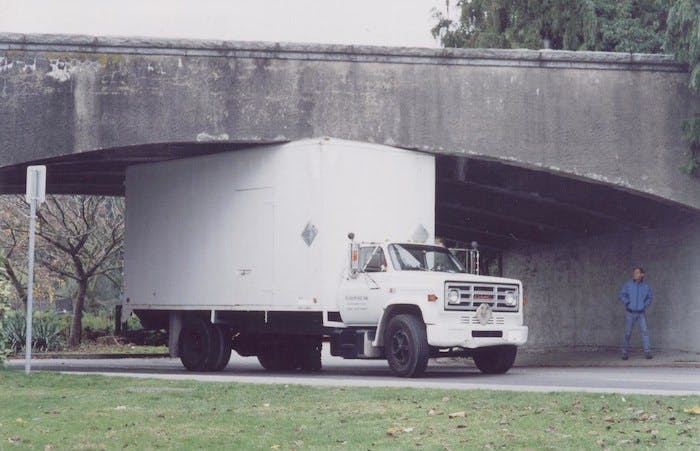 A large white truck stuck under bridge