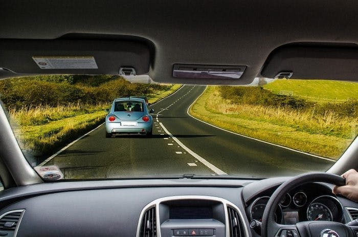 An image from the inside of a car of a road ahead and another car on the road 