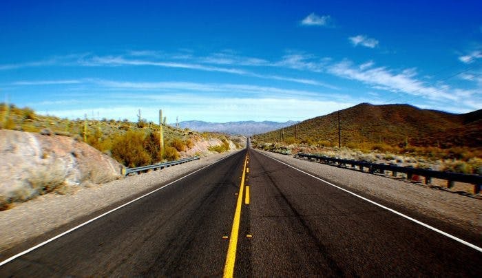 An image of a long stretch of road with desert around it 