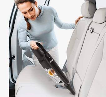 An image of a woman cleaning the backseat of a car with a hoover