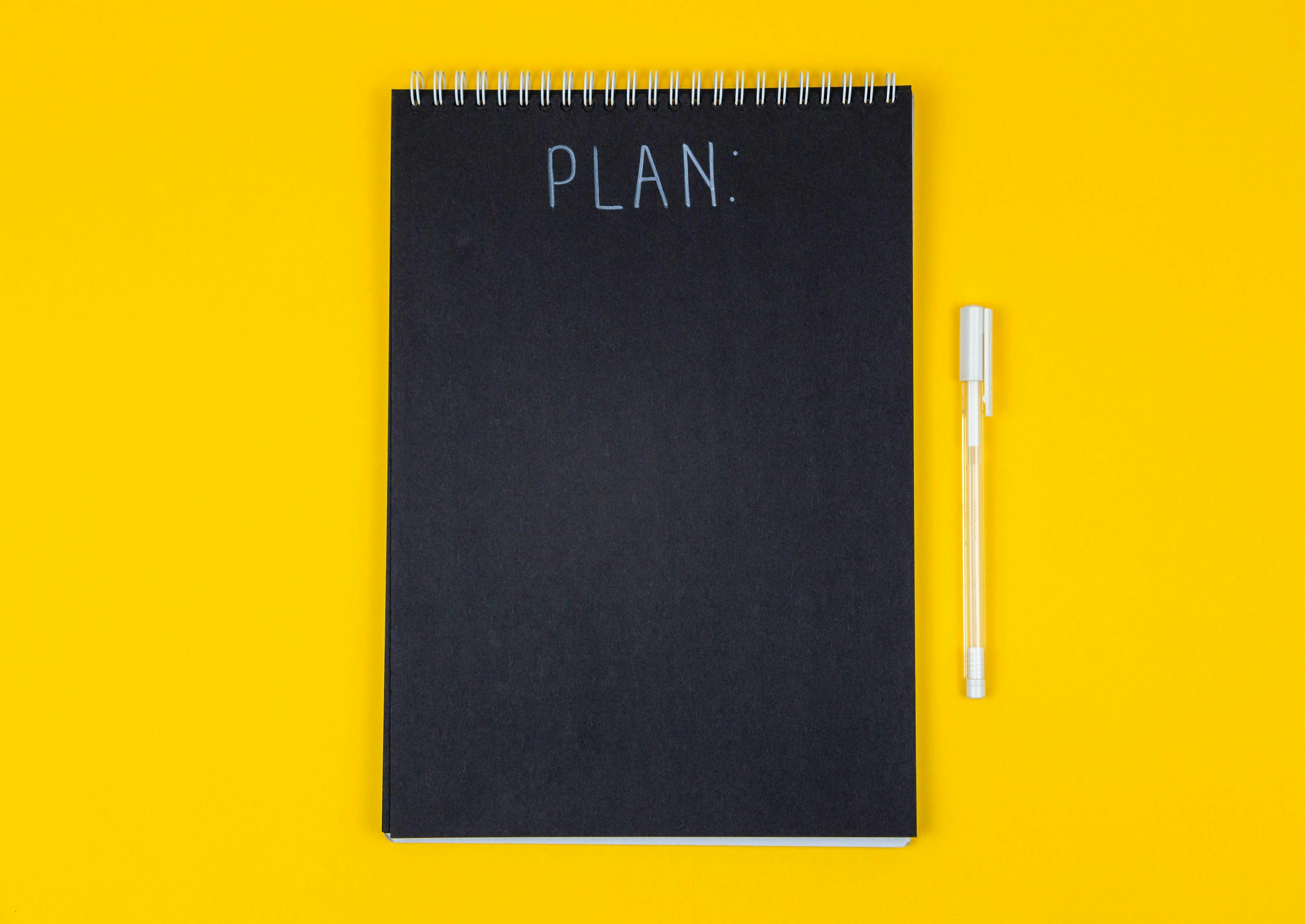 a black rectangular notepad with the word PLAN written on it