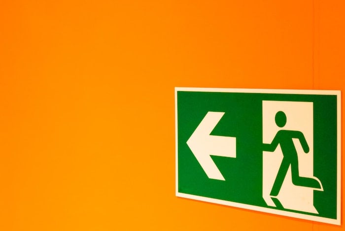 Green exit sign of figure running towards arrow on a yellow background