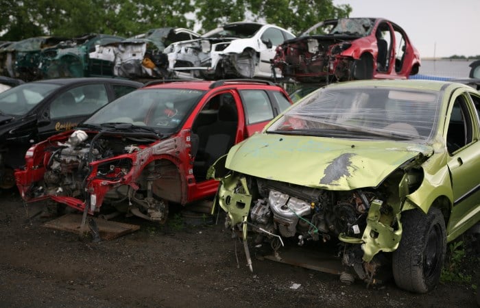 Scrapped red and green cars next to each other in a scrap yard