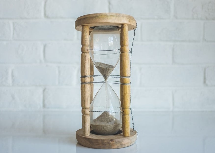Wooden hourglass with white sand against white brick backdrop