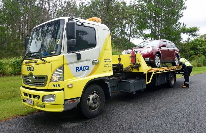 Yellow and white tow truck with a red car on the back