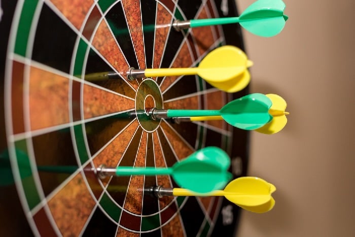 Side angle shot of dartboard with multiple yellow and green darts stuck in it