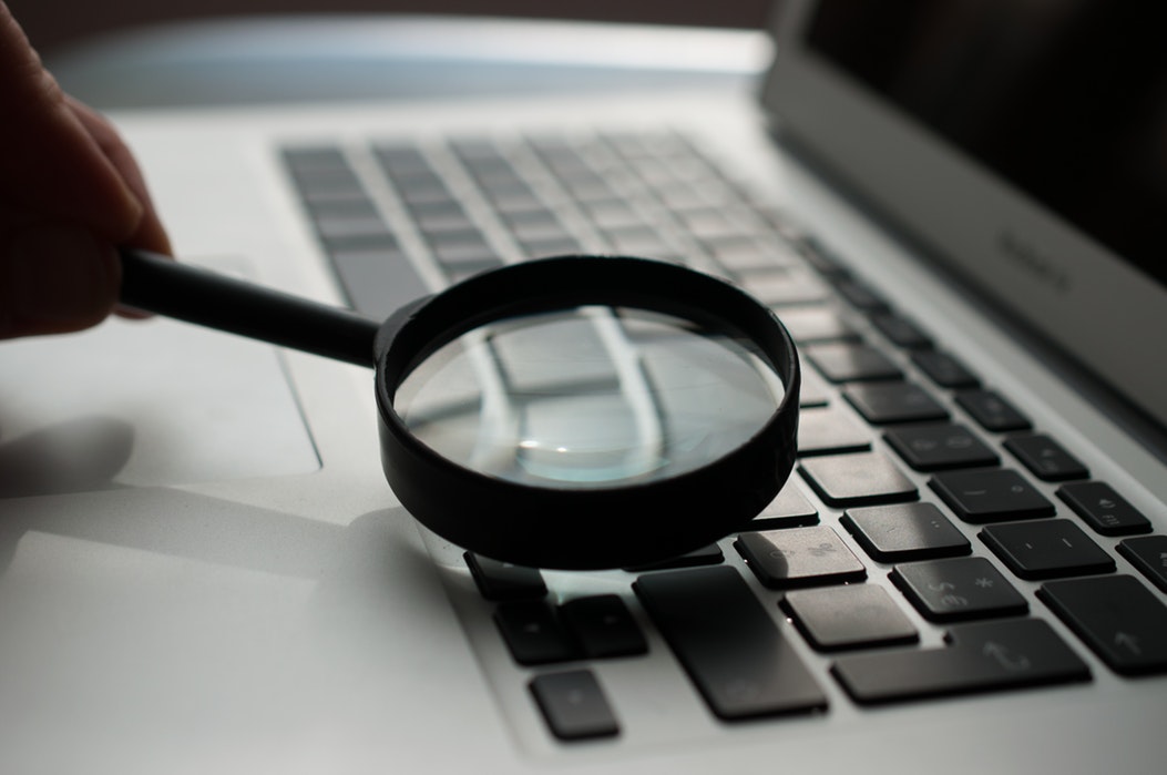 Magnifying glass held over the keyboard of a laptop with black keys