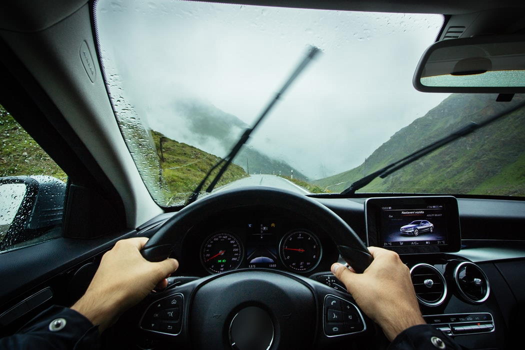 Hands on steering wheel of car driving through rain